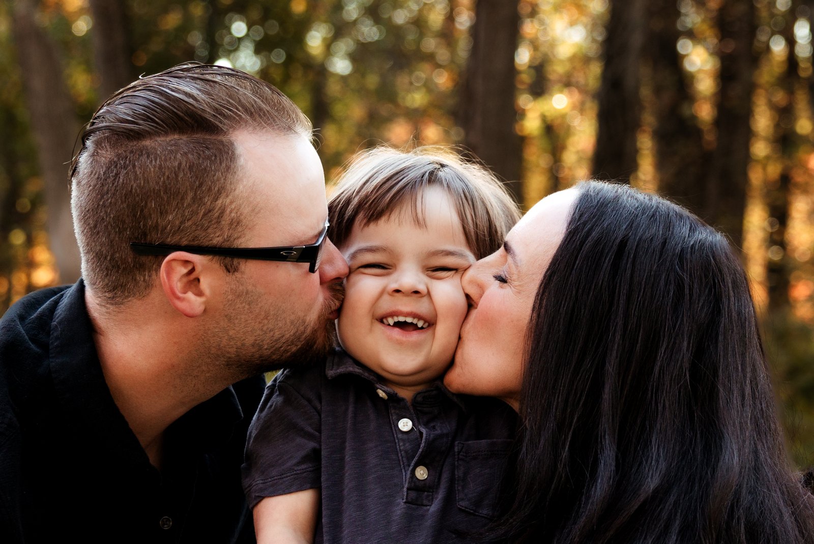 Close up of Mom and Dad giving their toddler son a kiss on his cheek.