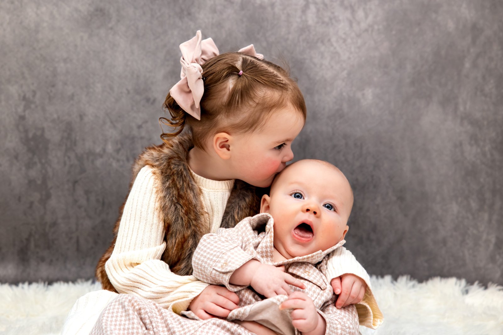 Close up of younger sister holding her baby brother and giving him a kiss on the forehead.