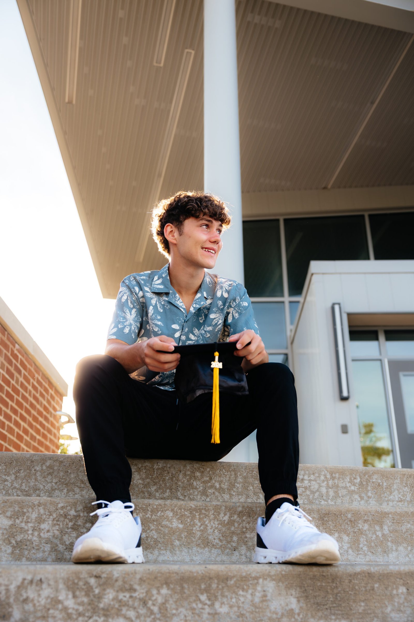 zach_highschoolgrad-16 High school senior outdoor portraits sitting on steps in front of school with grad cap.