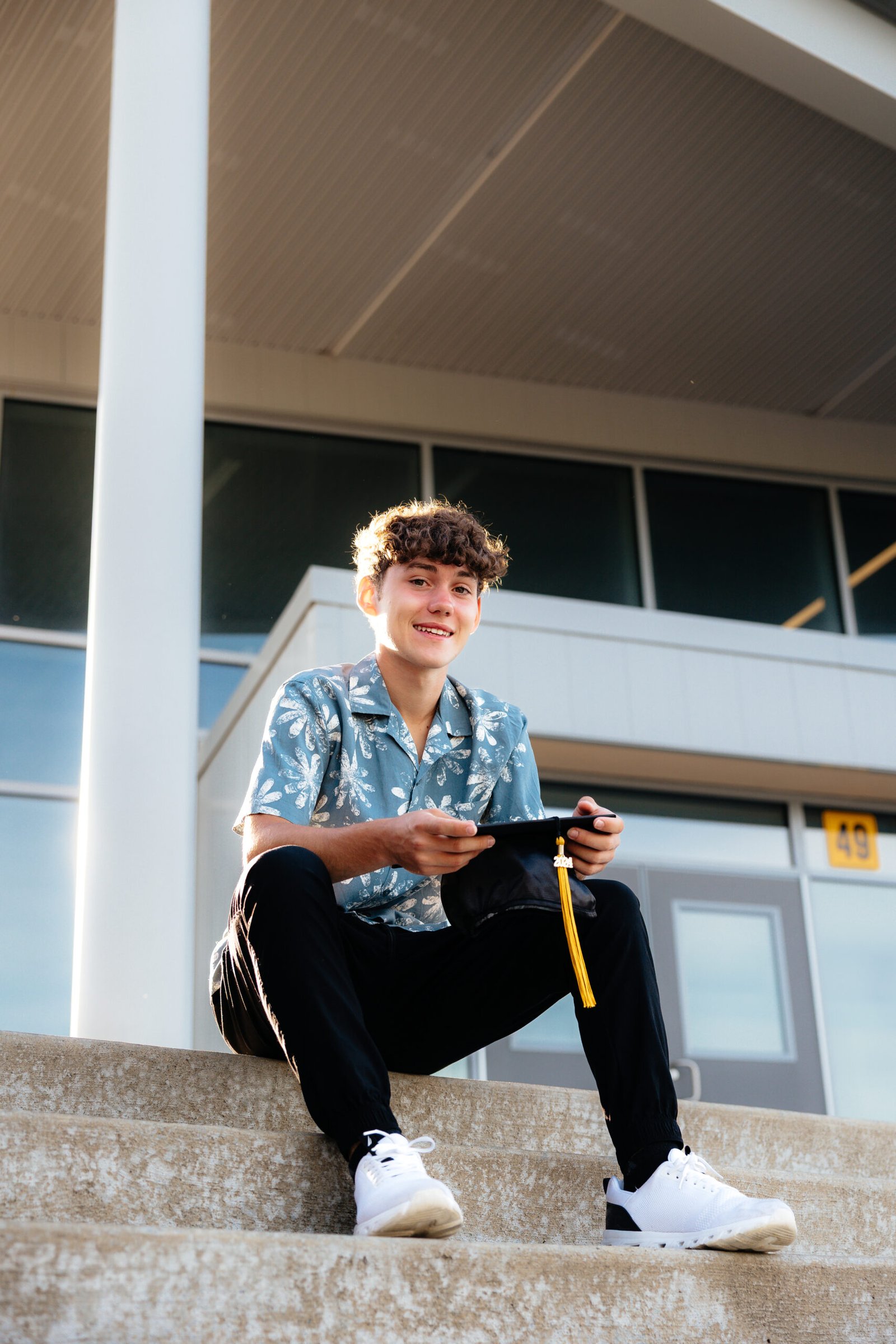 zach_highschoolgrad-17 High school senior outdoor portraits sitting on steps in front of school with grad cap.