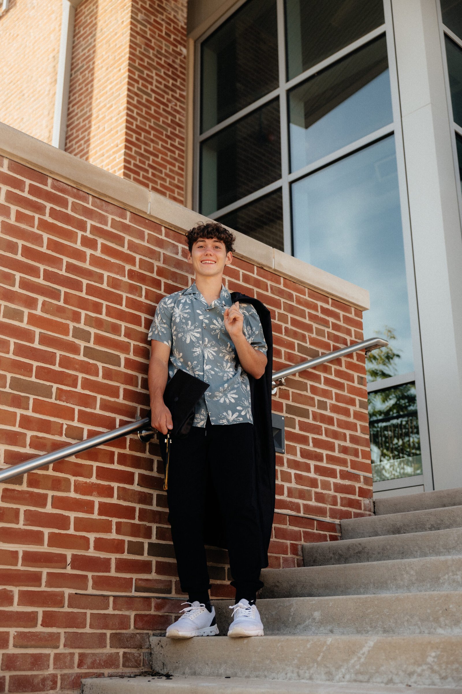 zach_highschoolgrad-21 High school senior standing on school steps holding his cap and gown.